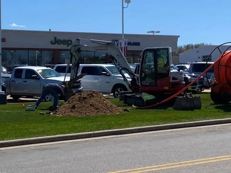 Crew and excavator working on a commercial lawn to install well and conduit lines in West Allis, WI