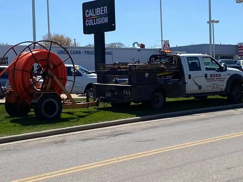 Herr Directional Drilling service truck and a trailer-mounted spool of orange conduit staged at a job site