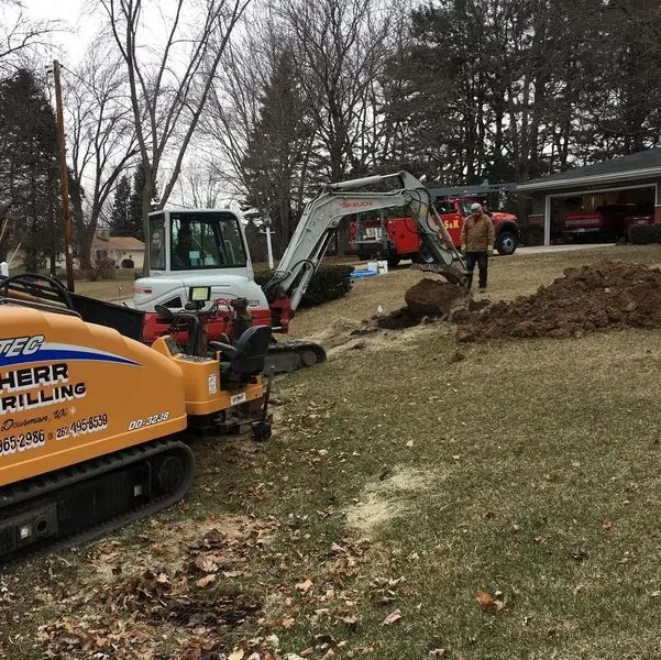 Herr Drilling directional drill and excavator working together across a residential front yard
