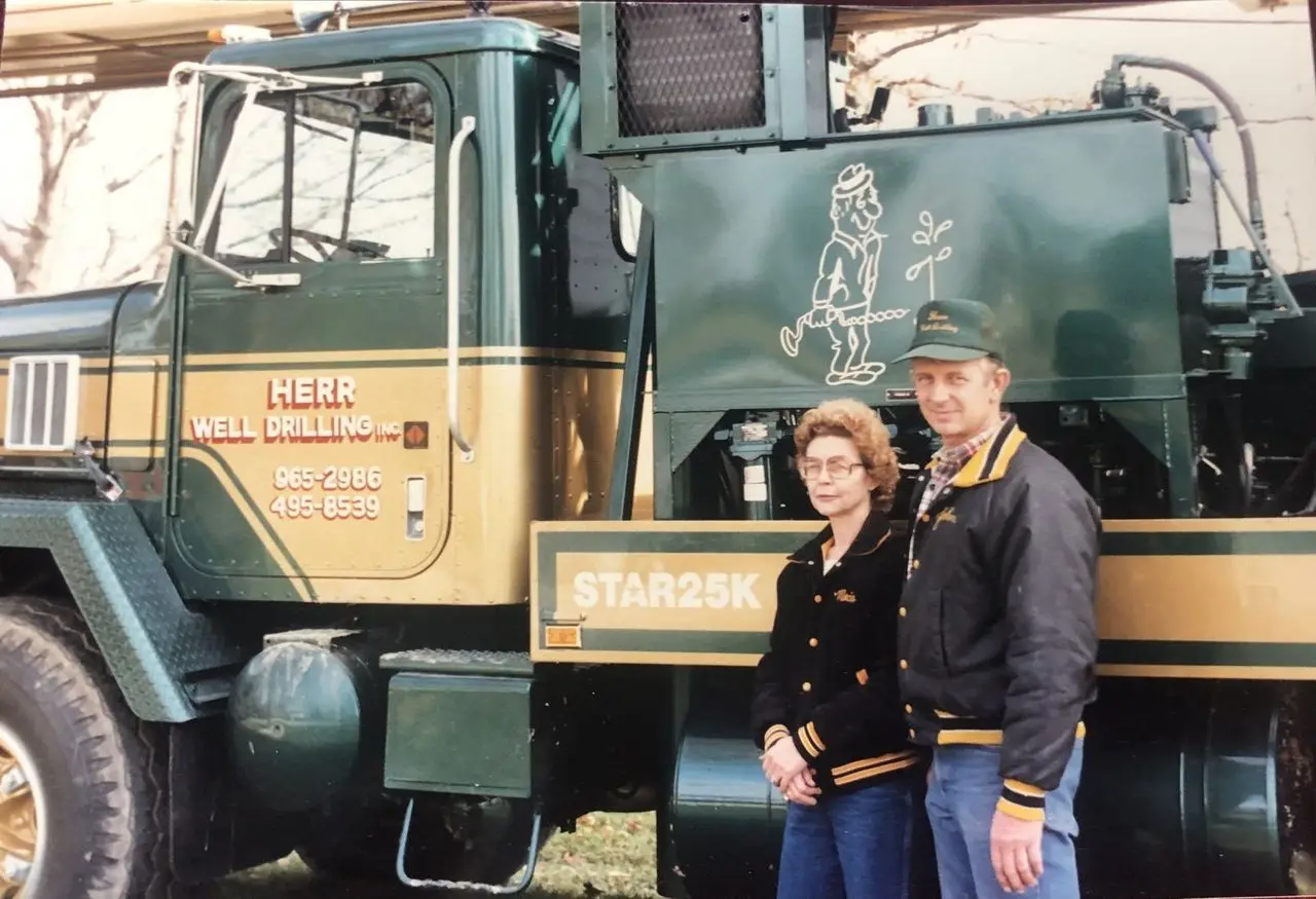 Founder John C. Herr Jr. and a woman standing beside the green and gold Herr Well Drilling Star 25K rig truck.
