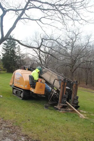 Operator running a tracked directional drill rig anchored on an open wooded lot