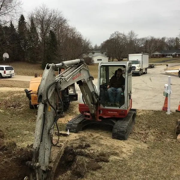 Excavator digging a utility trench in a residential yard for well and water line work in Brookfield, WI