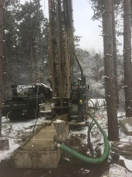 Herr Well Drilling rig drilling a residential well in snowy woods, winter work near Hartland, WI