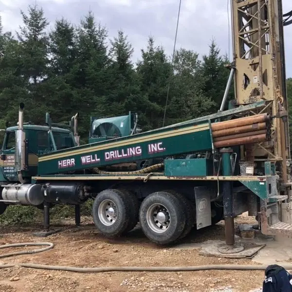 Green Herr Well Drilling truck drilling a residential well on a wooded lot near Wales, WI