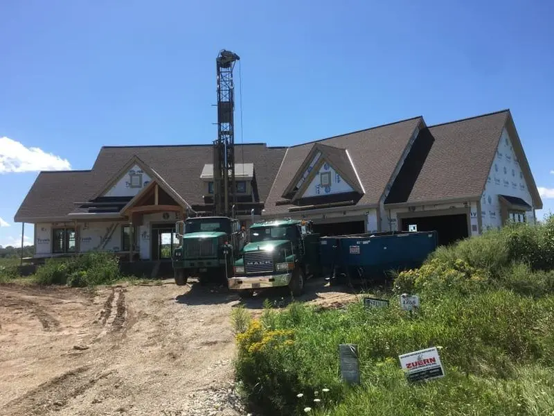 Herr Well Drilling rig and support truck drilling a new well at a house under construction