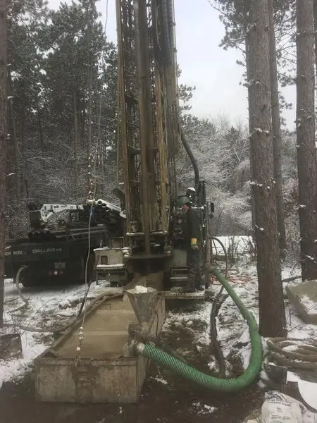 Herr Well Drilling rig running in snowy woods with the discharge hose feeding a settling tub