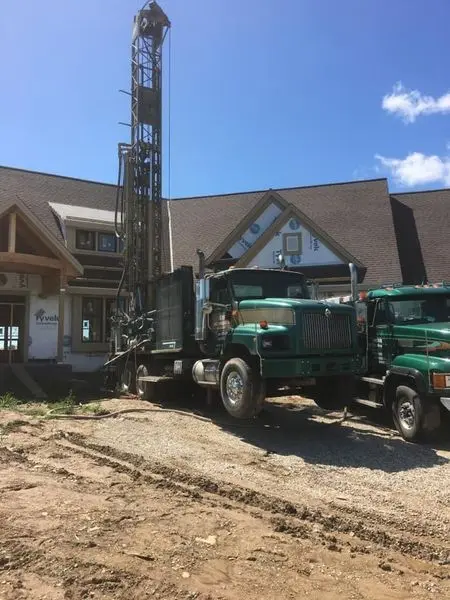 Green Herr Well Drilling rig truck drilling alongside a new home still under construction